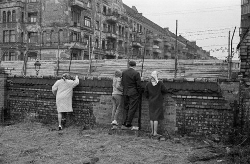 People Look Over Barb Wire at Berlin Wall
